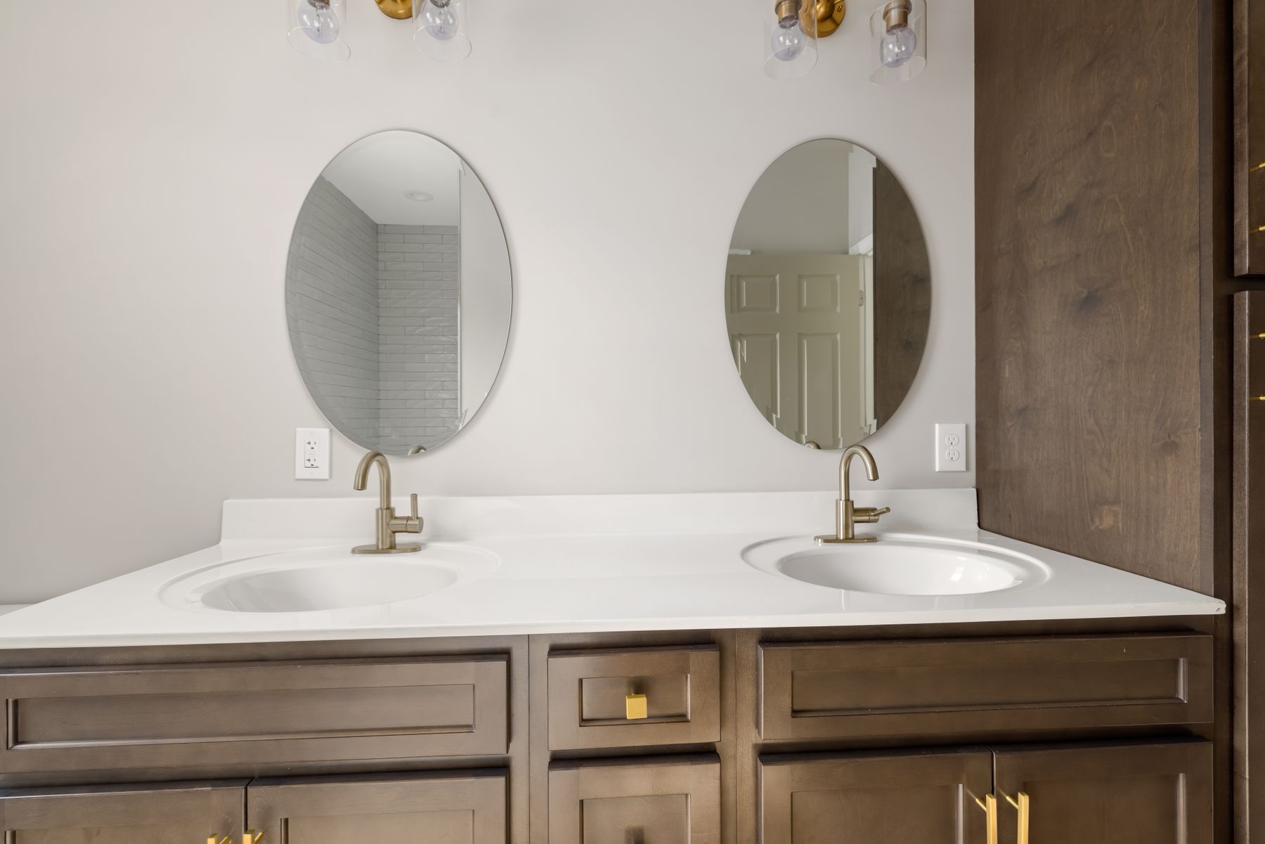 Double bathroom vanity with brass faucets and oval mirrors